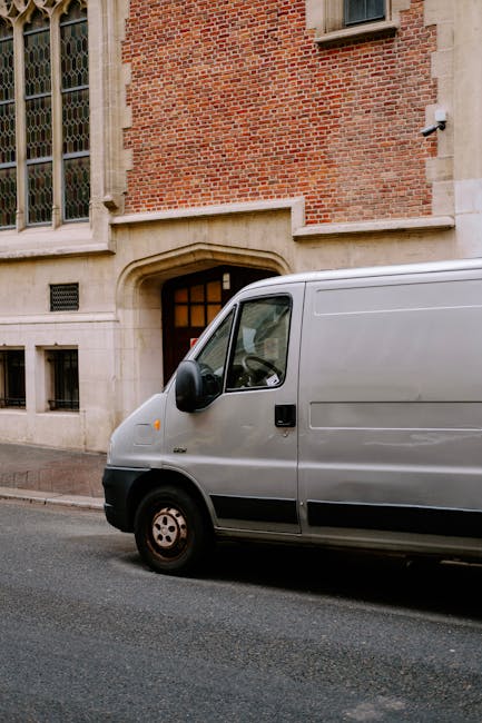 Two movers from Man with Van Ruislip are engaged in a home relocation task, standing behind a black van with its rear doors wide open on a paved street. They are carefully loading or unloading a large